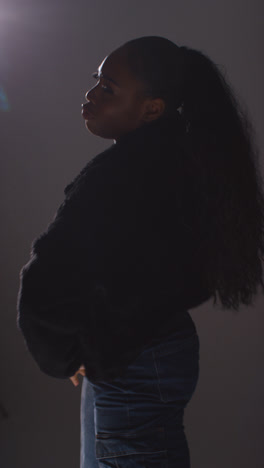 Vertical-Video-Backlit-Studio-Portrait-Shot-Of-Young-Woman-Dancing-Against-Grey-Background